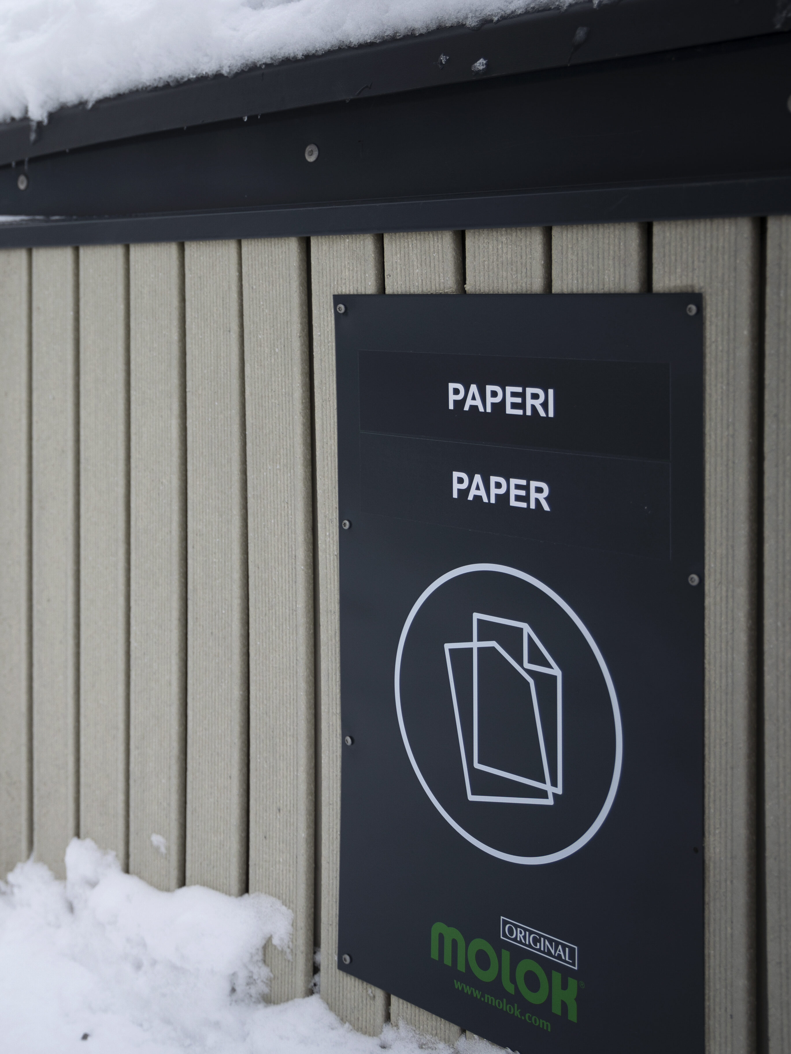 Kuvassa näkyy beigejä jäteastioita, joista etummaisessa lukee Paperi. On talvi ja lunta.